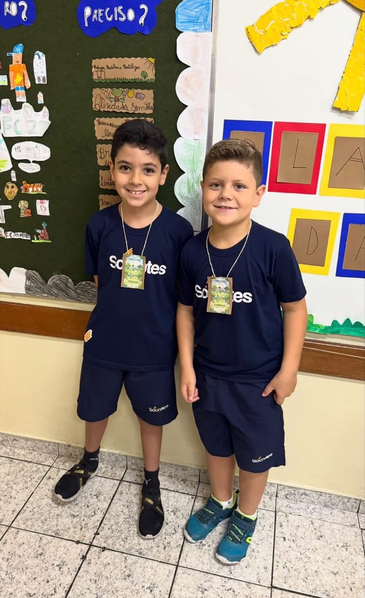 Dois alunos de uniforme e crachá prontos para atender na feira