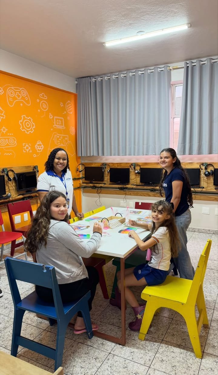 Alunas e professora em volta de uma mesa com material colorido durante a feira